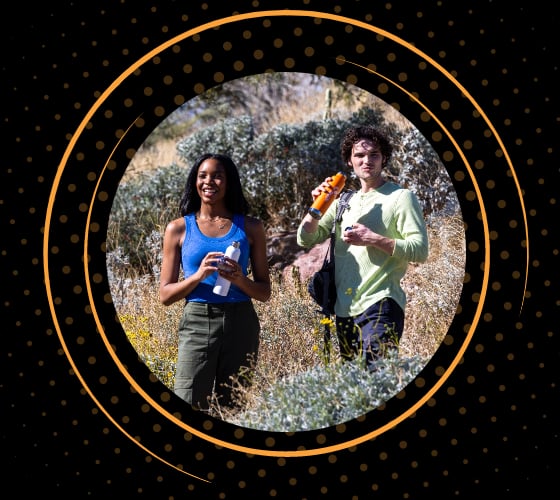 Dos excursionistas parados en un campo, haciendo una pausa para hidratarse.